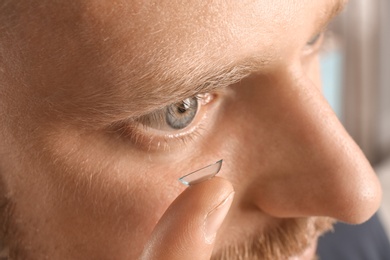 Photo of Young man putting contact lens into his eye, closeup