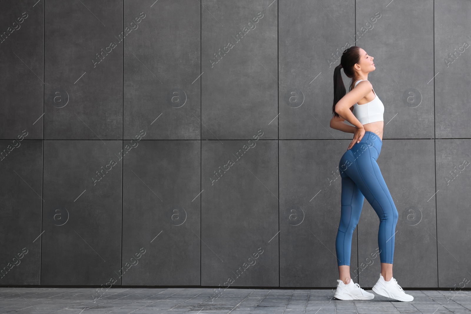Photo of Beautiful woman in sportswear near dark grey wall outdoors. Space for text