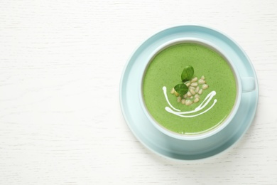 Cup of healthy green soup with fresh spinach on white wooden table, top view. Space for text