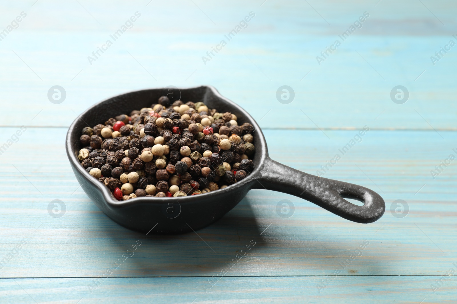 Photo of Aromatic spice. Different peppers in dish on light blue wooden table