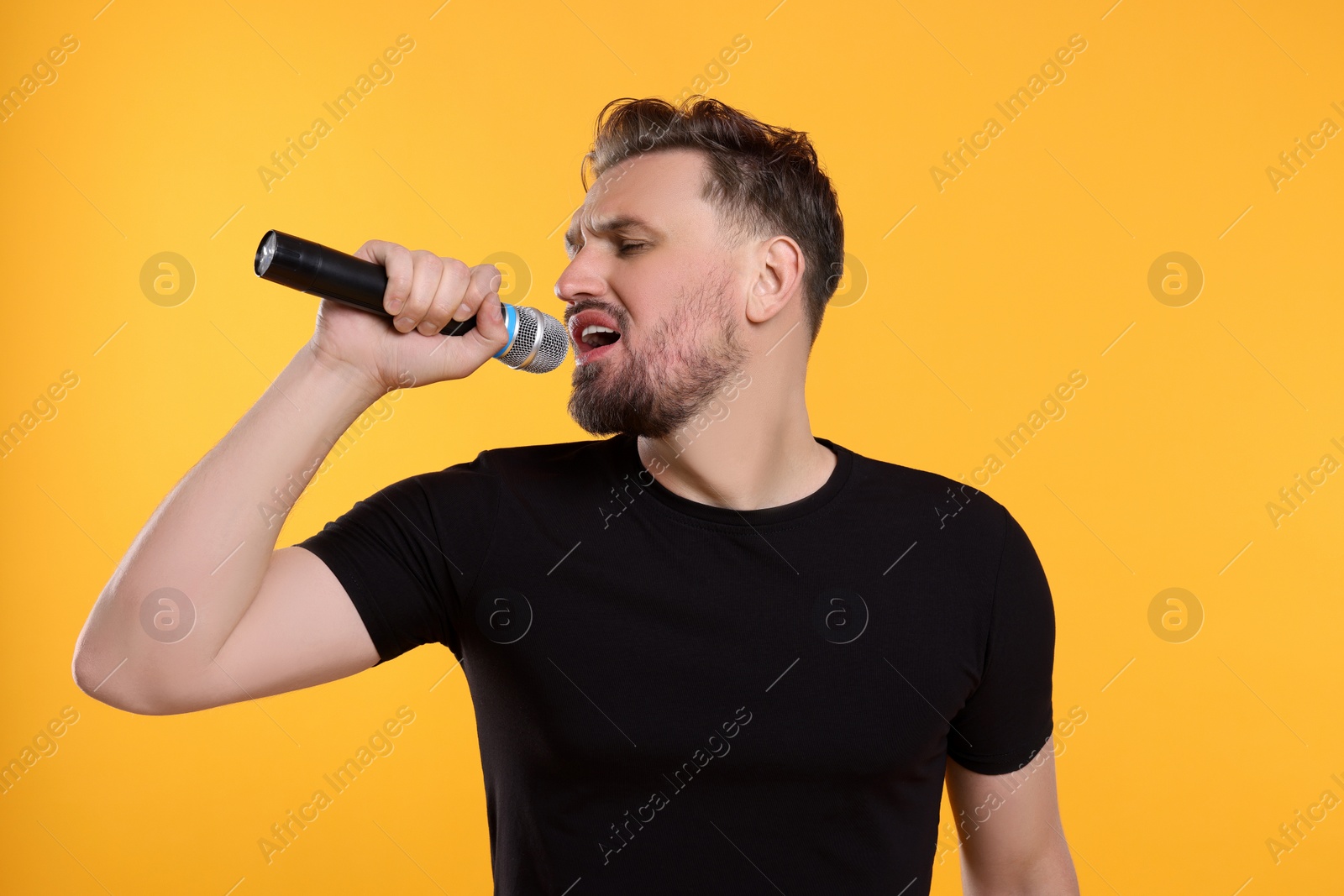 Photo of Handsome man with microphone singing on yellow background