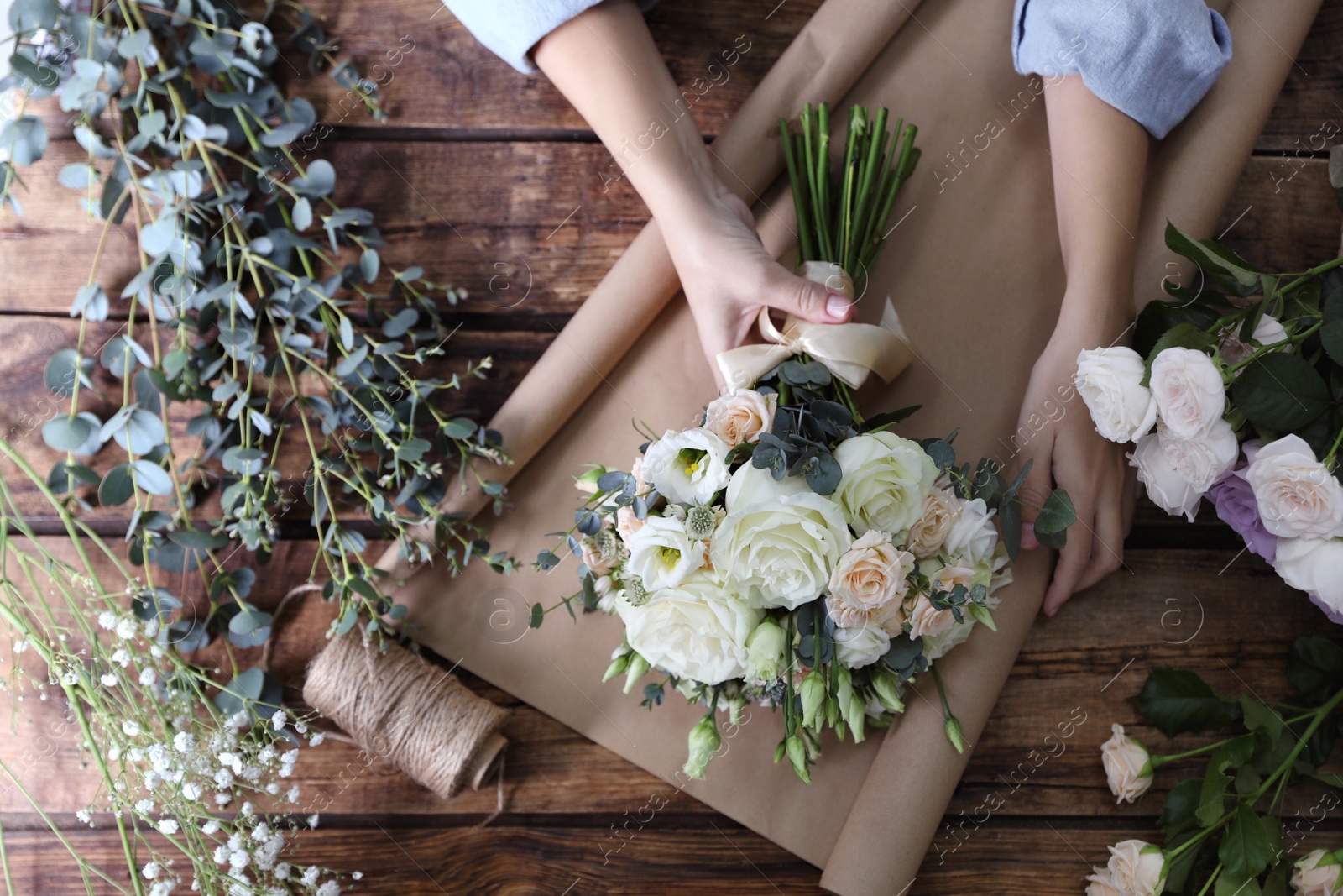 Photo of Florist wrapping beautiful wedding bouquet with paper at wooden table, top view