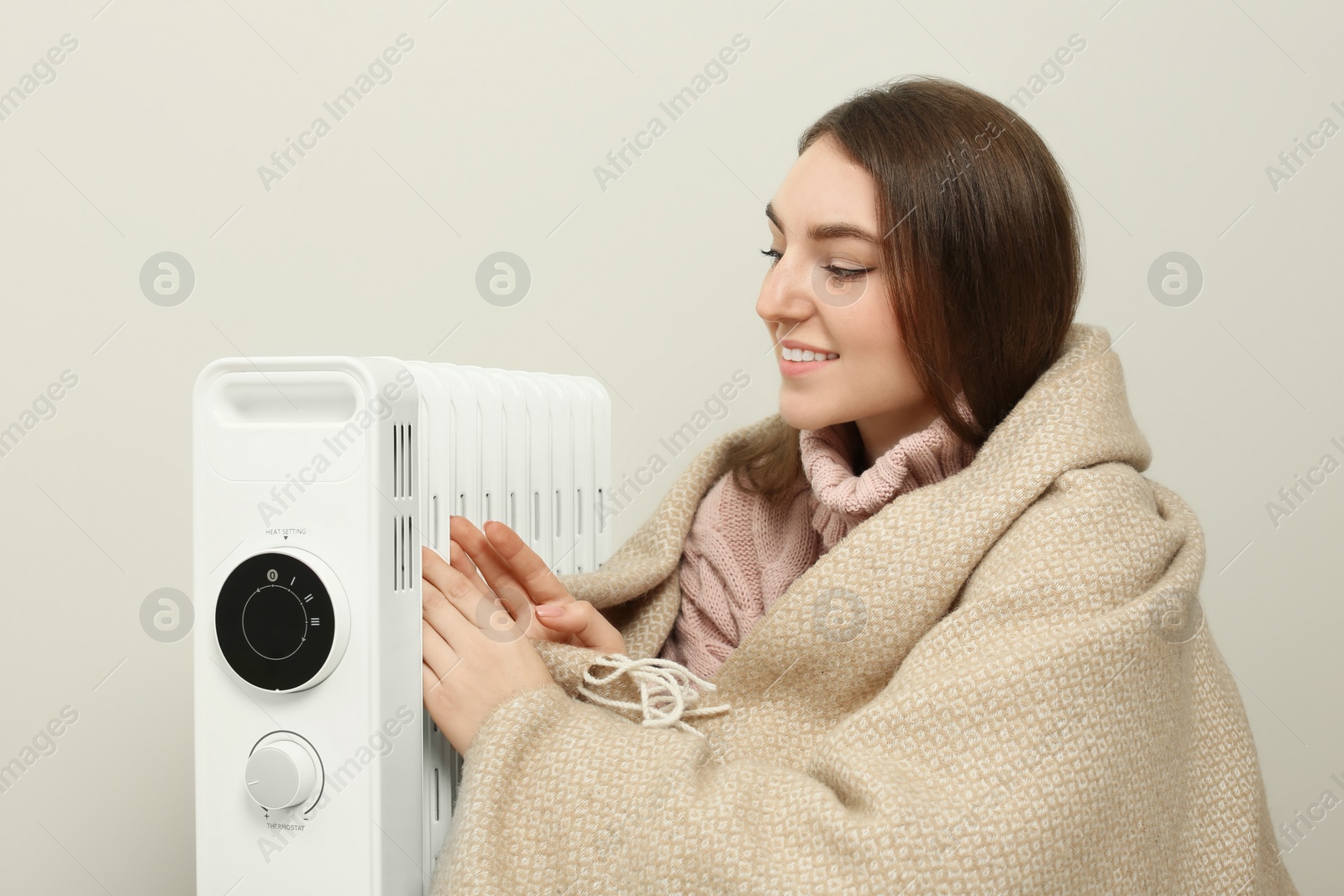 Photo of Young woman warming herself near modern electric heater indoors