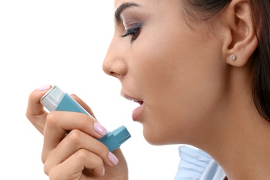 Young woman using asthma inhaler on white background, closeup