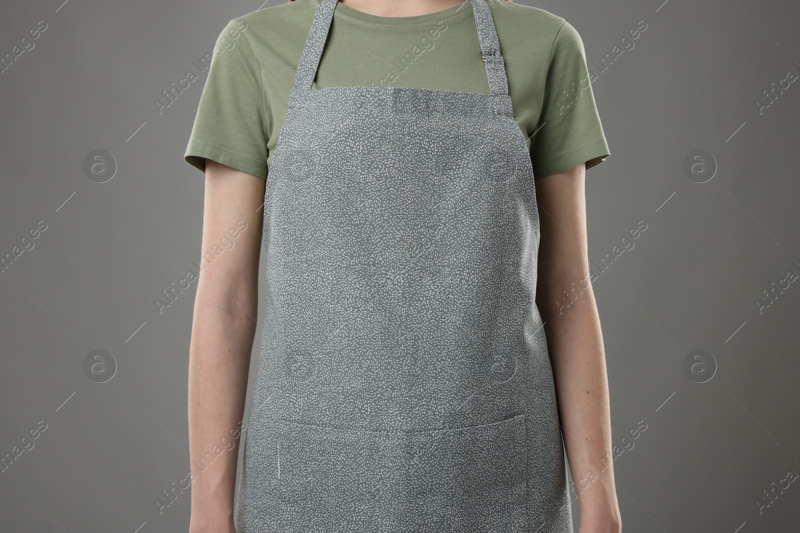 Photo of Woman wearing kitchen apron on grey background, closeup. Mockup for design