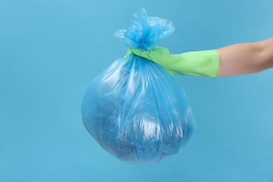 Photo of Woman holding plastic bag full of garbage on light blue background, closeup