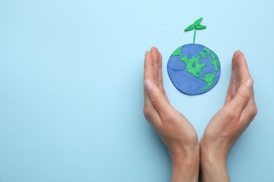 Photo of Woman near plasticine model of planet with green seedling and space for text on light blue background, top view. Earth Day