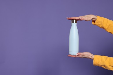 Photo of Woman holding thermos bottle on purple background, closeup. Space for text