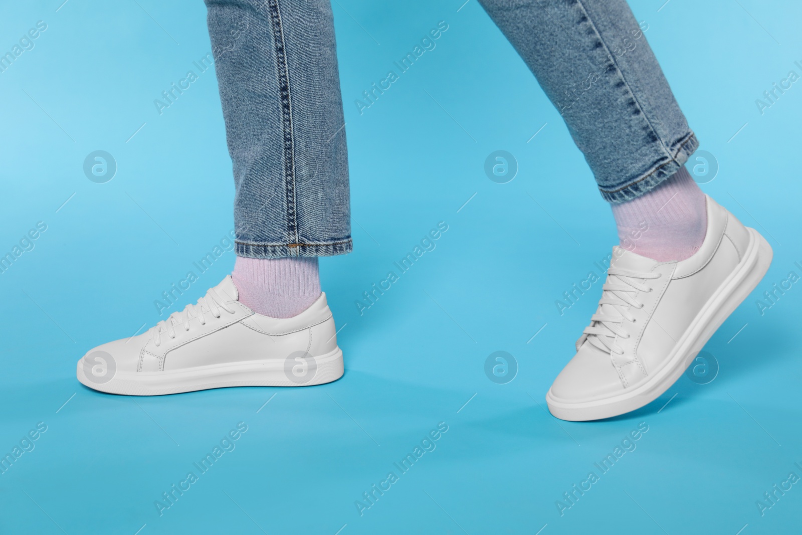 Photo of Woman wearing stylish white sneakers on light blue background, closeup