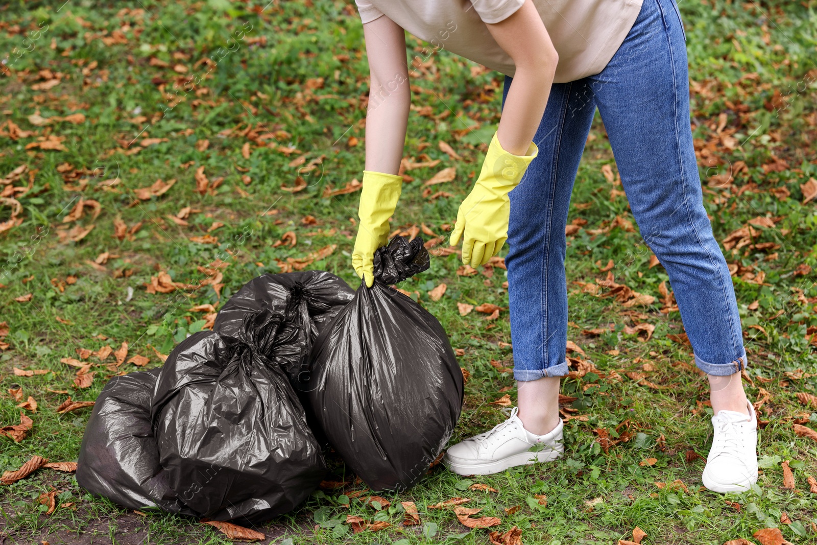 Photo of Woman holding plastic bags with garbage in park, closeup.