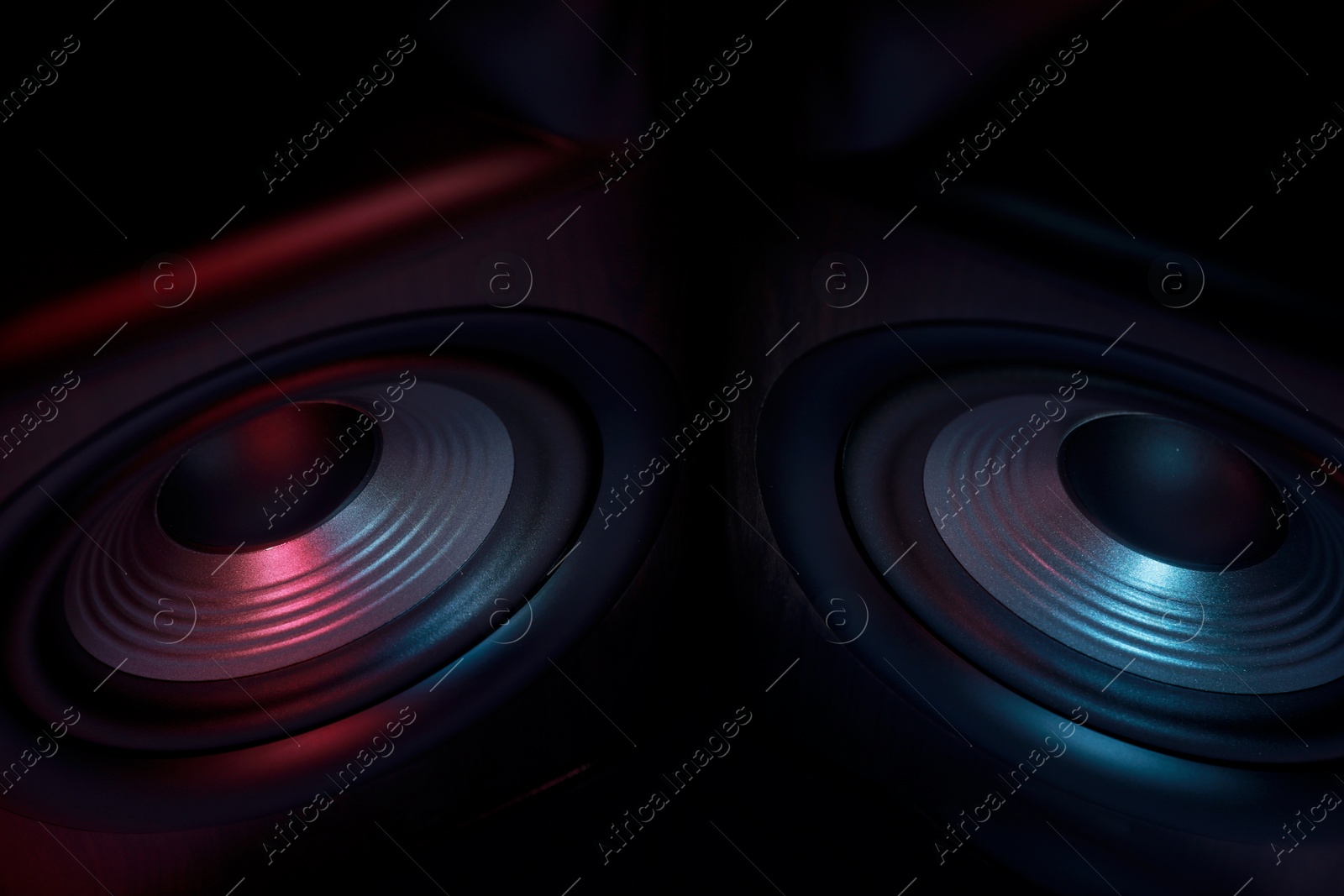 Photo of Modern sound speakers in neon light as background, closeup