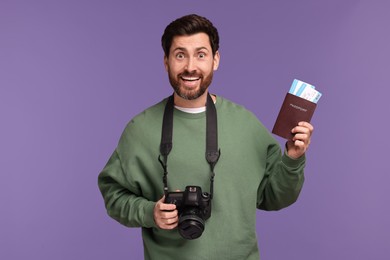 Smiling man with passport, camera and tickets on purple background