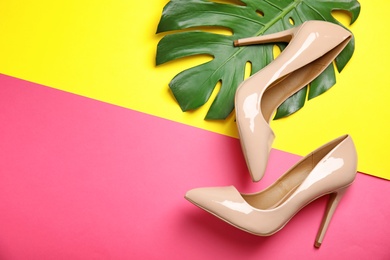 Photo of Pair of beautiful shoes with monstera leaf and space for text on color background, top view