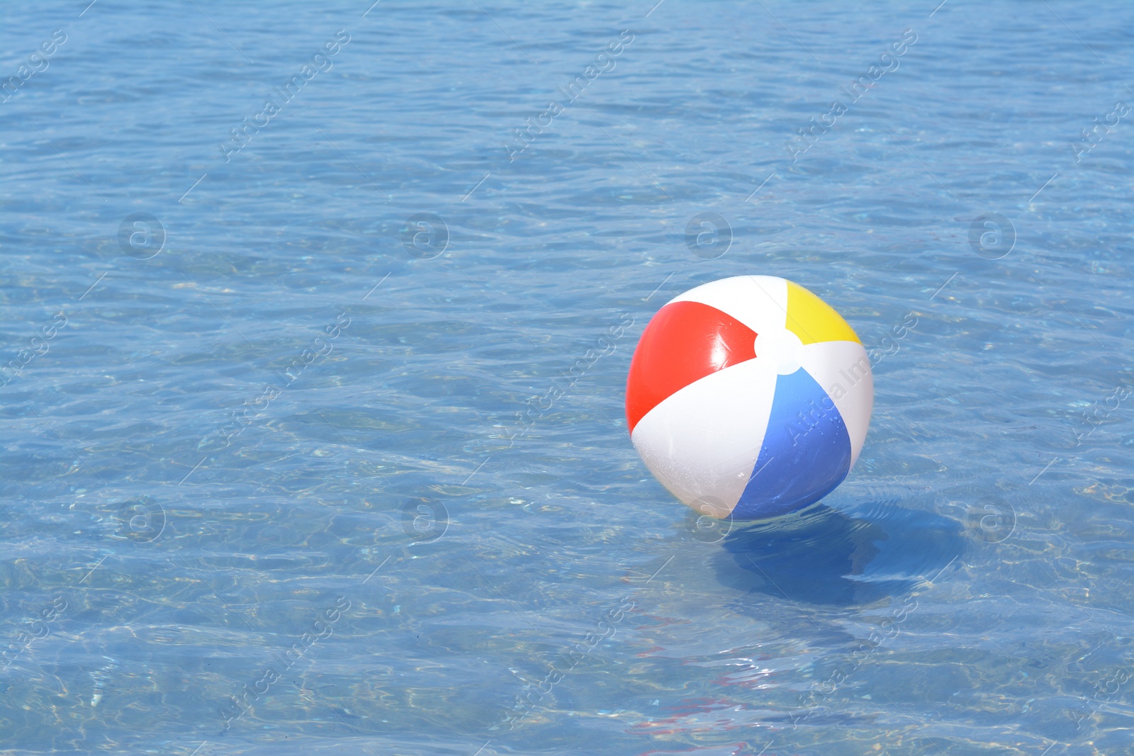 Photo of Colorful beach ball floating in sea on sunny day, space for text