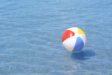 Photo of Colorful beach ball floating in sea on sunny day, space for text