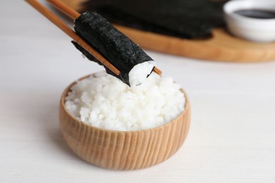 Photo of Chopsticks with cooked rice wrapped in nori sheet over white table, closeup