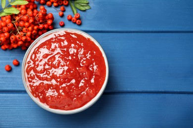 Photo of Delicious rowan jam and berries on blue wooden table, flat lay. Space for text