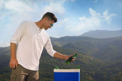 Photo of Man taking bottle of beer from cool box in mountains