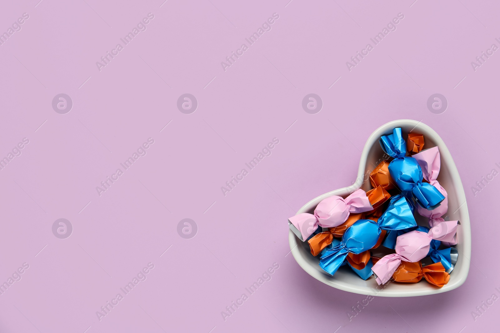 Photo of Candies in colorful wrapper on pink background, top view. Space for text