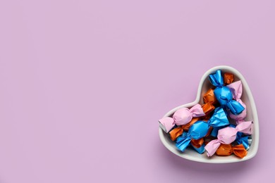 Photo of Candies in colorful wrapper on pink background, top view. Space for text