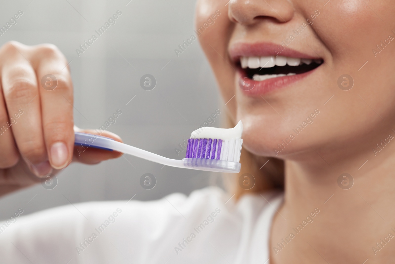 Photo of Woman holding brush with toothpaste in bathroom, closeup