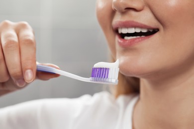 Woman holding brush with toothpaste in bathroom, closeup