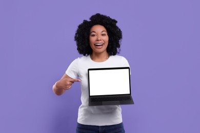 Happy young woman showing laptop on purple background