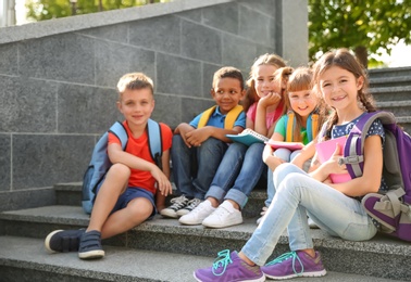 Photo of Cute little children with backpacks and notebooks outdoors. Elementary school