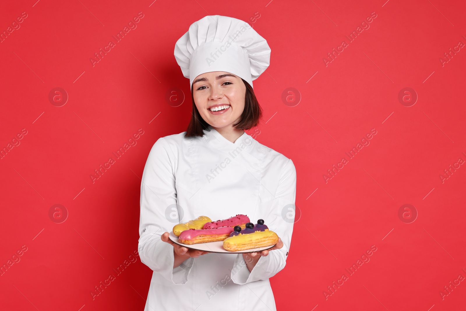 Photo of Happy confectioner with delicious eclairs on red background
