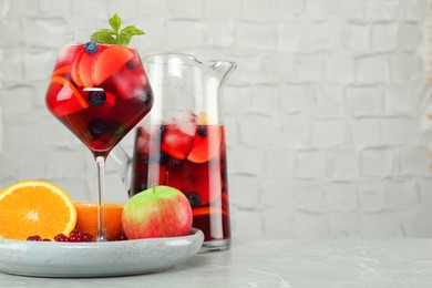 Photo of Glass and jug of Red Sangria with fruits on table near white brick wall, space for text