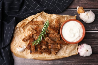Photo of Crispy rusks with rosemary and sauce on wooden table, flat lay