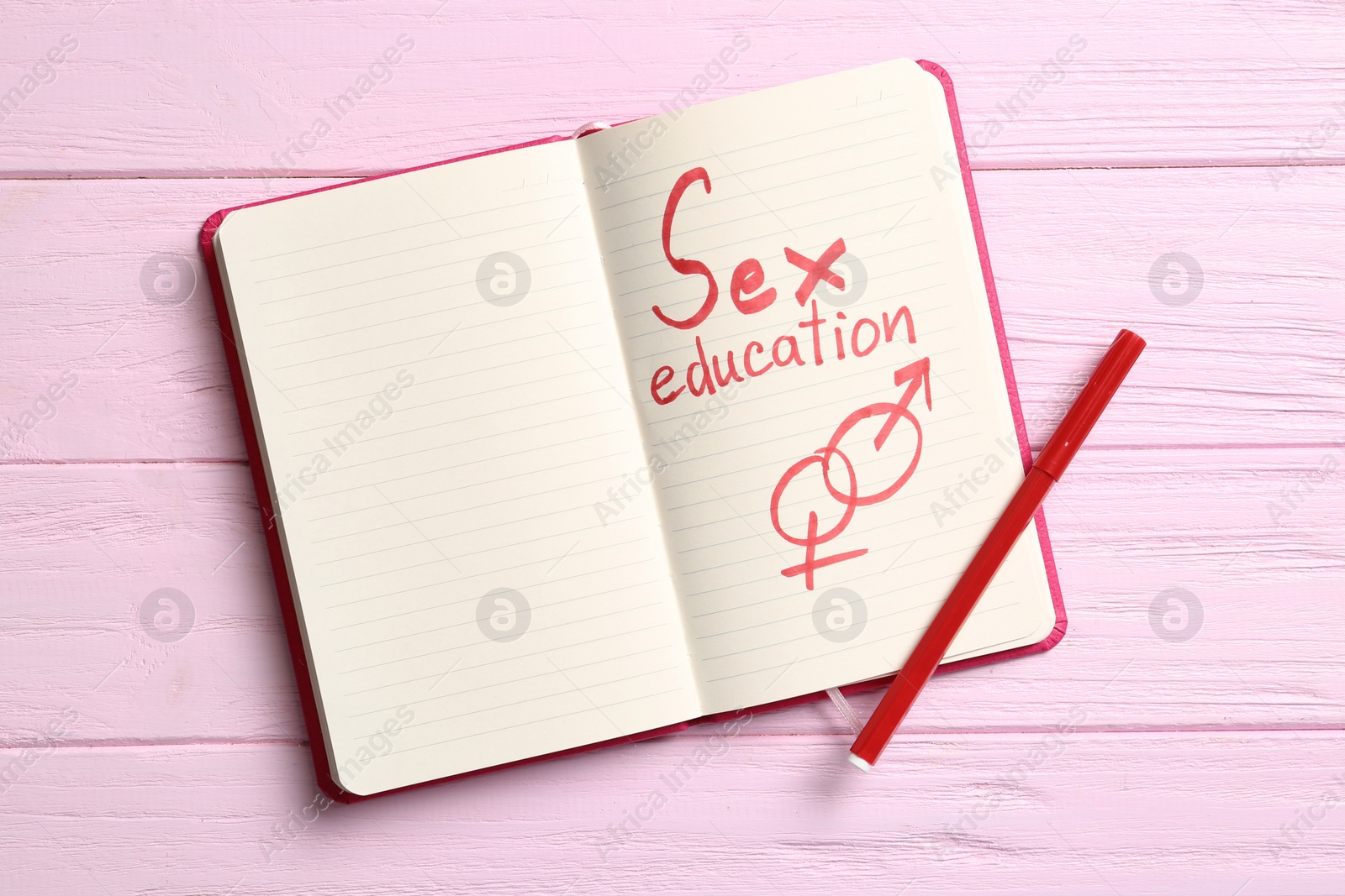 Photo of Notebook with phrase "SEX EDUCATION" and gender symbols on pink wooden background, top view. Space for text