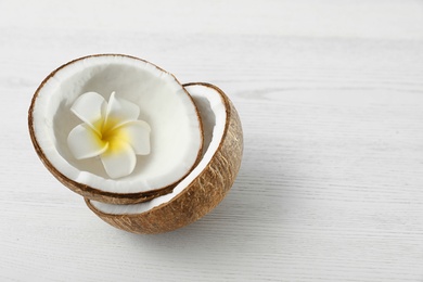 Photo of Halves of coconut and flower on white wooden background. Space for text