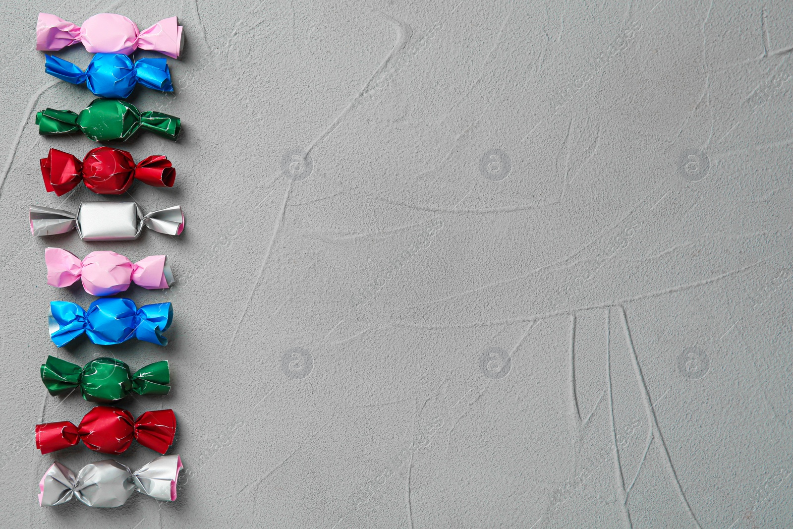 Photo of Candies in colorful wrappers on grey table, flat lay. Space for text