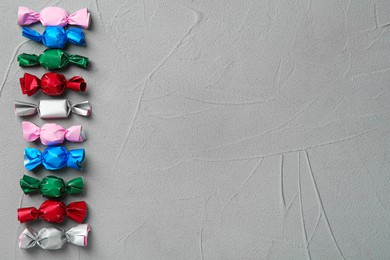 Photo of Candies in colorful wrappers on grey table, flat lay. Space for text