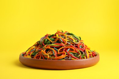 Photo of Plate of spaghetti painted with different food colorings on yellow background