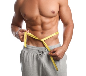 Young man with slim body using measuring tape on white background, closeup view