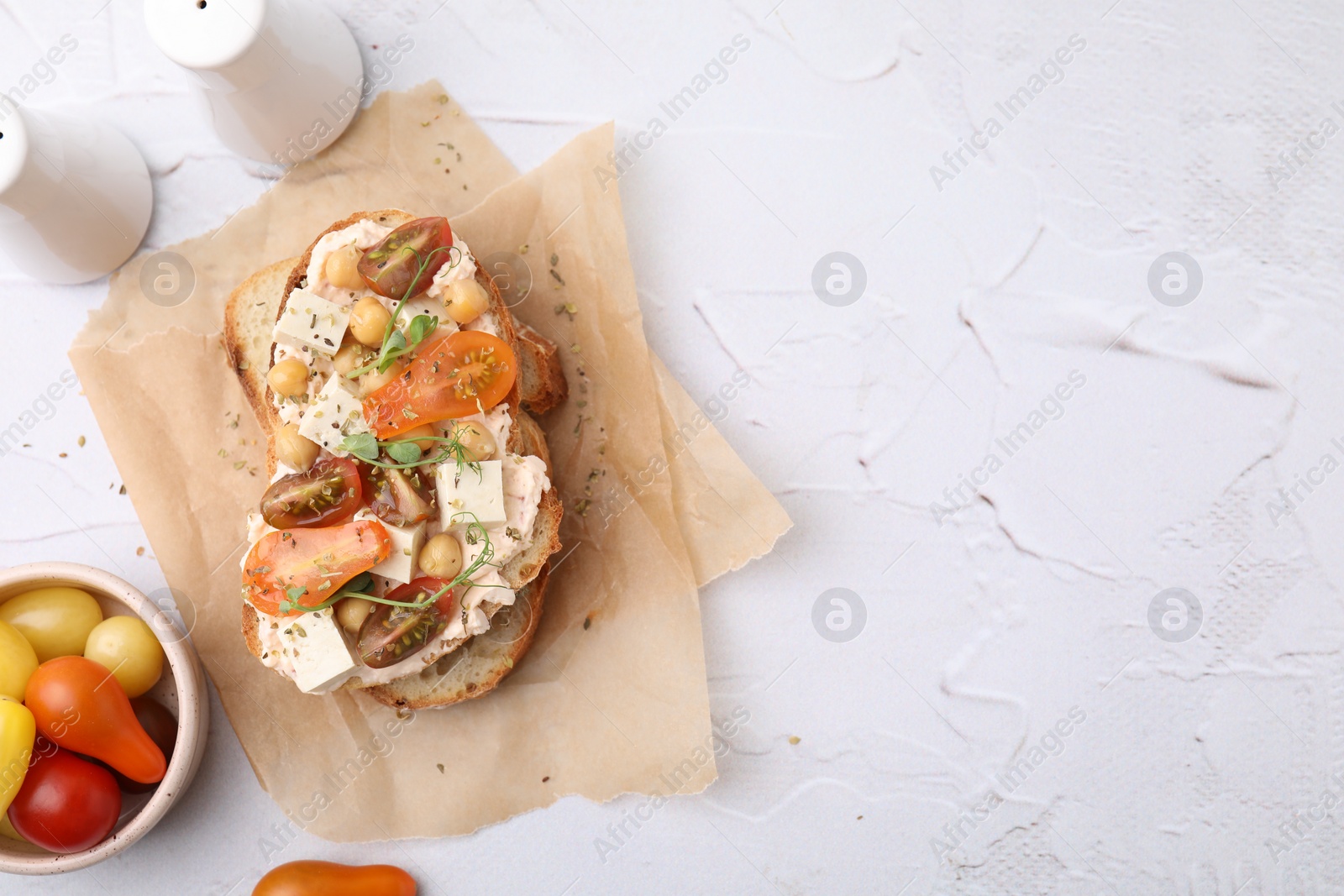 Photo of Tasty vegan sandwich with tomatoes, tofu and chickpeas on white textured table, flat lay. Space for text