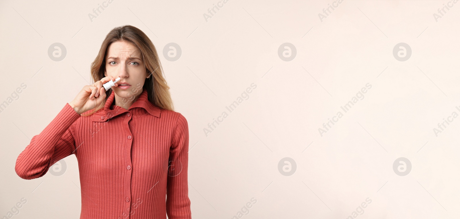 Photo of Sick young woman using nasal spray on beige background. Space for text