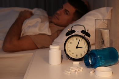 Man suffering from insomnia in bed at night, focus on pills and alarm clock