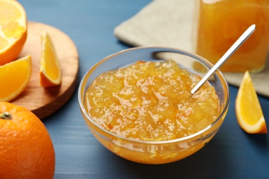 Photo of Delicious orange marmalade in bowl on blue wooden table