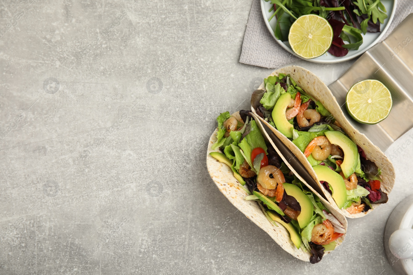 Photo of Delicious tacos with shrimps, avocado and lime on light grey table, flat lay. Space for text