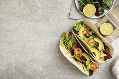 Delicious tacos with shrimps, avocado and lime on light grey table, flat lay. Space for text