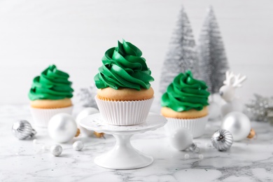 Photo of Delicious cupcakes with green cream and Christmas decor on white marble table