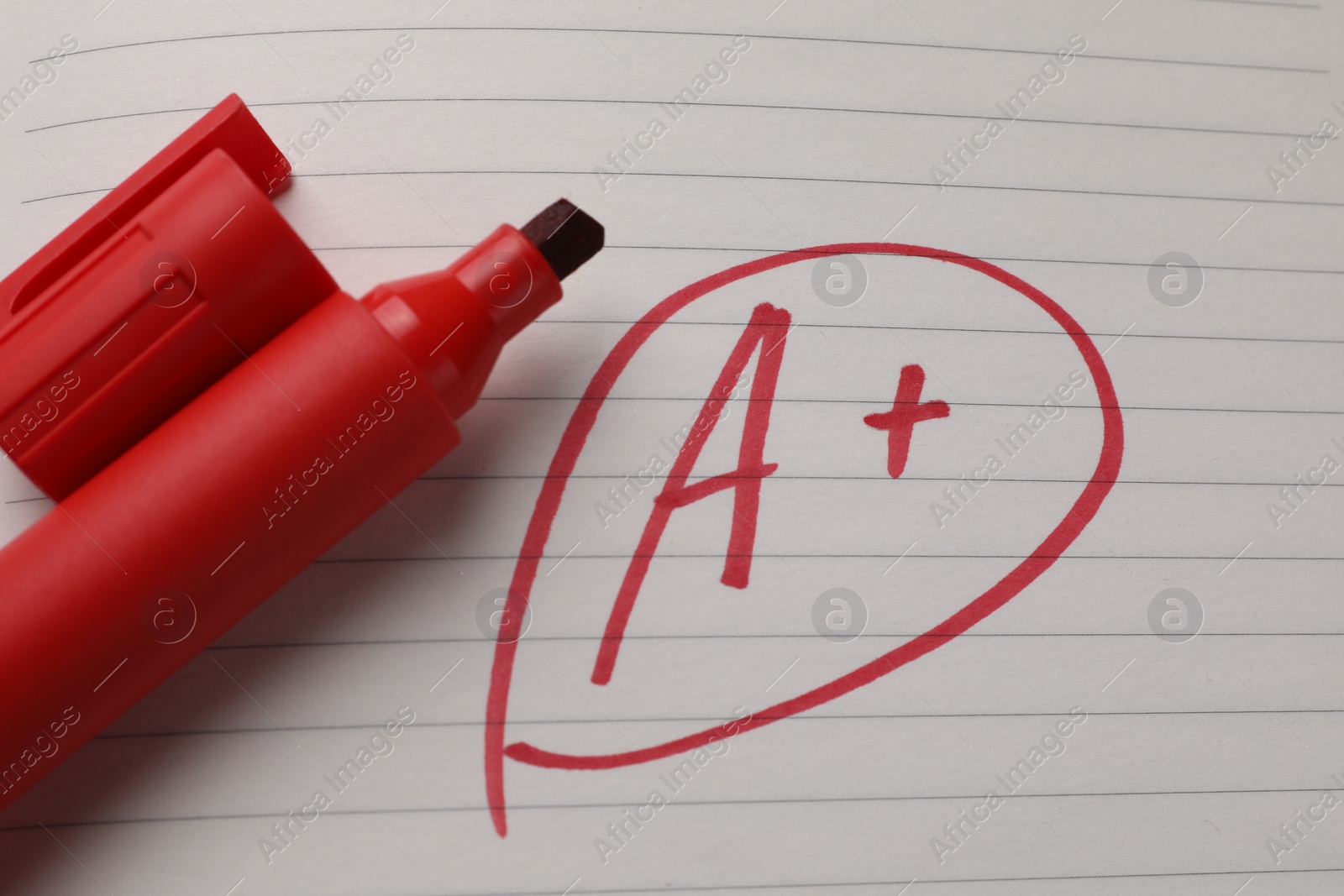 Photo of School grade. Red letter A with plus symbol on notebook paper and marker, top view