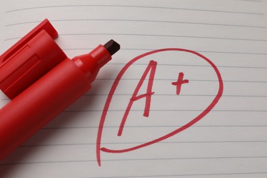 Photo of School grade. Red letter A with plus symbol on notebook paper and marker, top view