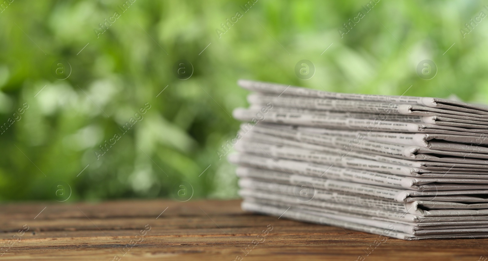 Photo of Stack of newspapers on wooden table against blurred green background, space for text. Journalist's work