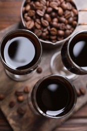 Shot glasses with coffee liqueur and beans on wooden table, top view