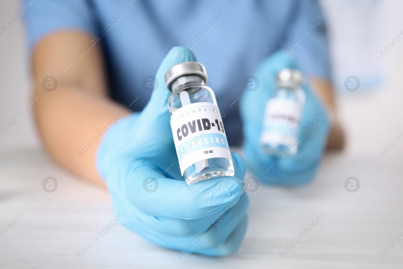 Photo of Doctor holding vial with vaccine against Covid-19 at table, closeup