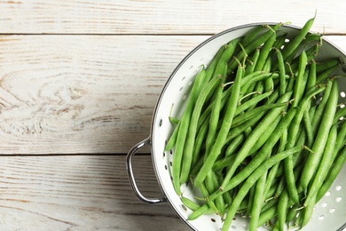 Photo of Fresh green beans in colander on white wooden table, top view. Space for text